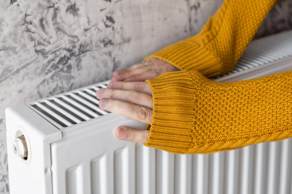 Person in a yellow sweater warming hands on a white radiator, emphasizing heating comfort in home HVAC systems.